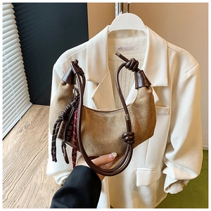 Détail d'un sac demi-lune en daim marron avec poignée en corde nouée et pompon