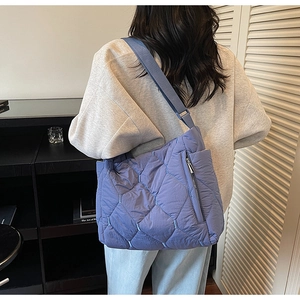 Rear view of model carrying a large quilted blue tote bag with wide shoulder strap
