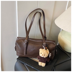 Detail of vintage brown cylinder bag featuring glossy PU leather and teddy bear charm