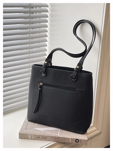 Detail of black lychee grain leather tote bag with gold hardware on a book prop