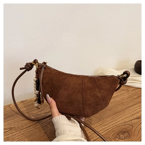 Close-up of brown suede croissant crossbody bag with decorative bead keychain accessory