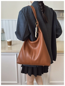 Close-up of brown pebbled leather tote bag with stylish charm on a minimal background