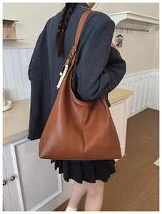 Detail of dark brown leather hobo bag with a beaded decorative pendant on the side