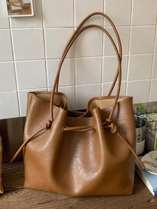 Brown leather tote bag with knotted shoulder straps and drawstring detail in home setting