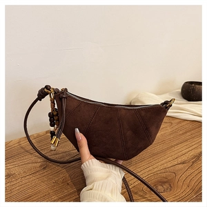 Detail of a dark brown suede crescent bag with leather strap and beaded charm on wood