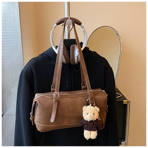 Close-up of brown Boston bag with lychee grain texture and a cute teddy bear charm detail