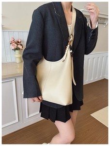 Detail of a large beige tote bag with decorative wooden beads on a black suit outfit