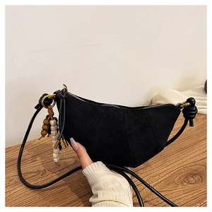 Close-up of black suede crescent bag with a decorative wooden bead charm on the zipper