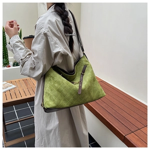 Close-up of green quilted suede tote bag with leather strap shown in an outdoor setting