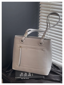 Close-up of light gray pebble leather tote bag with metal rings and zipper pocket detail