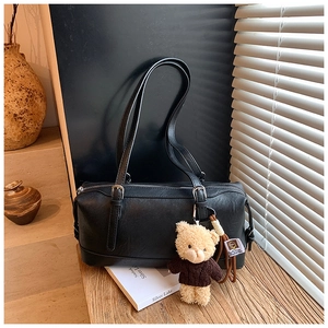 Close-up of black leather cylinder pillow bag with decorative teddy bear charm