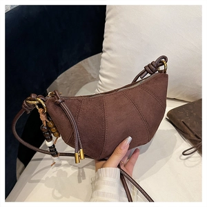 Close-up of brown suede crossbody bag featuring quilted seams and beaded charm detail