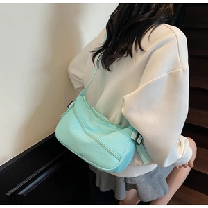Detail of mint green hobo bag with zipper accents and adjustable strap on a model