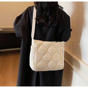 Detailed view of cream quilted nylon tote bag with large diamond stitching worn over black coat