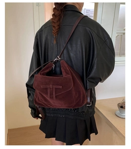 Detail of burgundy suede crossbody bag with iconic T-clasp on model in leather jacket
