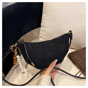 Detail of a black crescent crossbody bag in suede finish with retro beaded charm