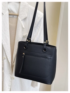 Detail of black lychee grain leather tote bag with gold hardware on white blazer background