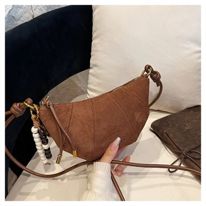 Detail of brown suede crescent bag featuring vertical stitching and beaded charm accessory