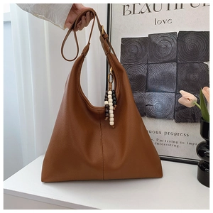 Detail of caramel brown tote bag with pebble texture and beaded charm on white table
