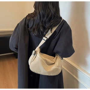 Detail view of a cream crescent crossbody bag with adjustable strap and metallic zippers