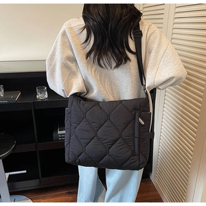 Detail view of the black quilted crossbody bag with adjustable wide fabric strap on a model