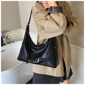 Detail of black pebbled leather hobo bag with gold zippers worn by a model in a modern room