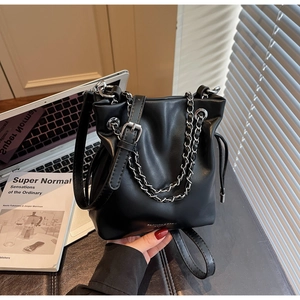 Detail of black leather bucket bag with silver chain and drawstring design in office setting