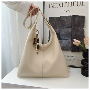 Detail of off-white leather hobo bag with litchi grain texture and bead tassel charm