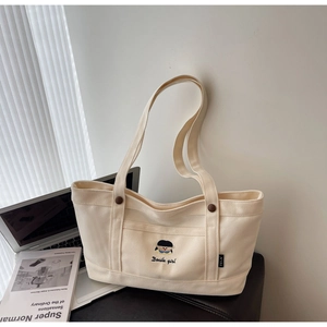 Detail der cremeweißen Canvas-Tasche mit Docile Girl-Stickerei und braunen Knöpfen