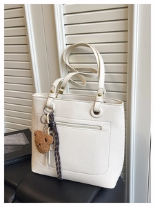 Detail of white lychee leather tote bag with brown bear charm and front zipper pocket