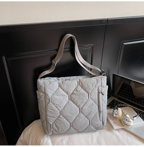 Detail of grey quilted tote bag featuring adjustable strap and side zipper pocket