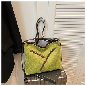Detail of green quilted suede tote bag with dark brown leather straps on a suitcase