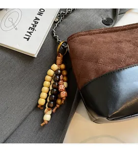 Détail du sac seau en daim matelassé et cuir avec chaîne et pompon en perles de bois