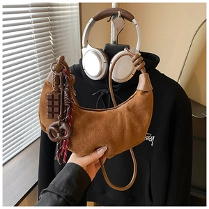 Gros plan d'un sac demi-lune en daim marron avec des breloques en chocolat