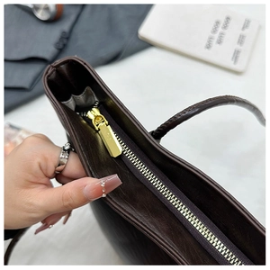 Detail view of smooth metal zipper and gray interior compartment of brown tote bag