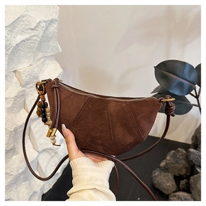 Detail of dark brown suede crescent bag featuring wooden bead charm and gold zipper