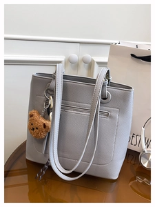 Detail of light gray lychee grain leather tote bag with zip pocket and bear charm
