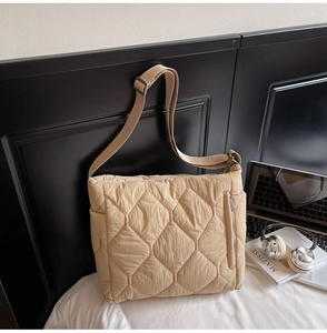Detail of beige quilted tote bag with adjustable strap next to laptop and headphones