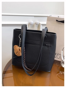 Detail of black pebbled leather tote bag with front zipper pocket and plush bear charm