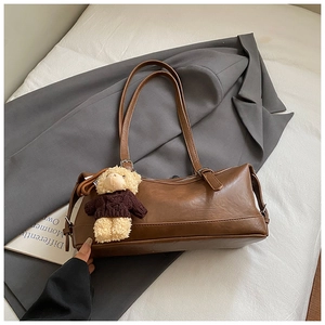 Close-up of retro brown shoulder bag with a cute teddy bear charm on white bedding