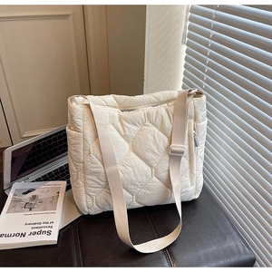 Detail of white quilted tote bag featuring adjustable strap and side zipper pocket