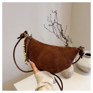 Detail of a brown suede crescent bag featuring wooden bead charms and a knotted strap