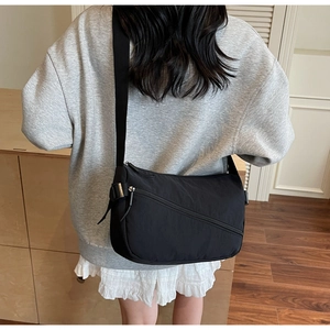 Detail of adjustable strap and front diagonal zipper on black nylon crossbody messenger bag
