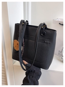Detail of black pebbled leather tote bag with side zipper pocket and brown bear charm