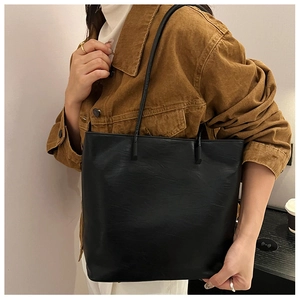 Detail view of the black textured leather tote bag worn by a model in a minimal setting