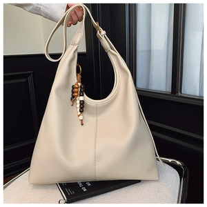 Detail of beige pebbled leather tote bag featuring a decorative wooden bead pendant