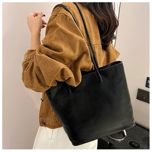 Close-up of black leather tote bag worn with a brown jacket for a daily commute look