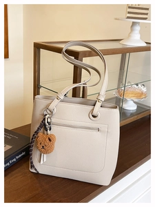 Detail of beige tote bag with litchi texture, front zipper pocket, and bear charm