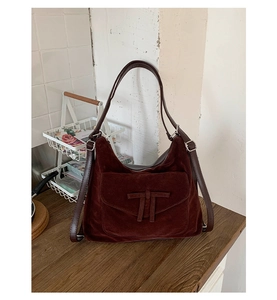 Detailed close-up of dark brown suede shoulder bag with leather trim and silver metal buckle