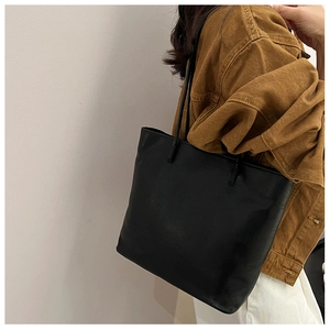 Minimalist black leather tote bag with long straps worn on shoulder for daily commute
